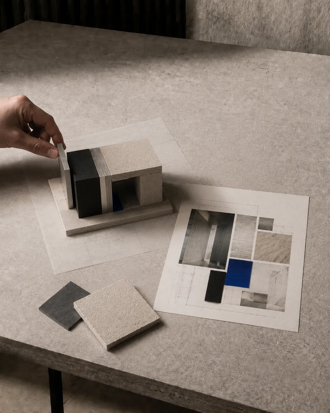 A hand makes a final adjustment to a small architectural prototype beside a resolved material composition.